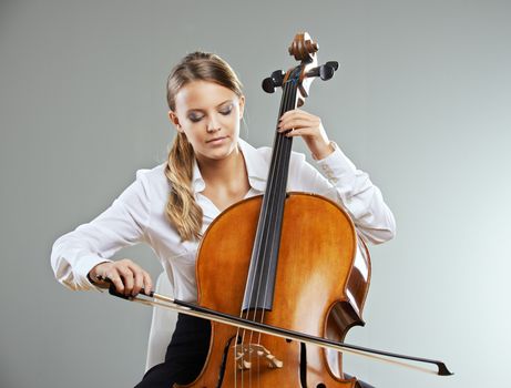 Beautiful young woman cellist on grey background