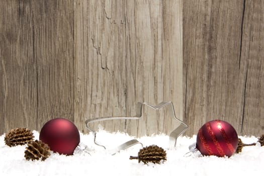 christmas decoration with wooden background, snow, christmas baubles red, shooting star, and pine cones 