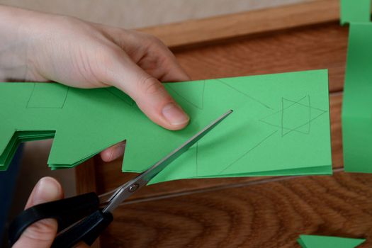 Closeup of cutting a Christmas tree shape from folded green paper