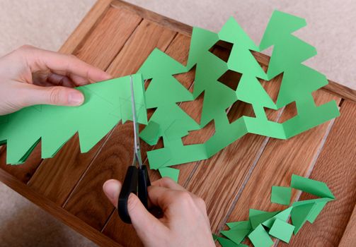 Cutting green card with scissors to make a chain of Christmas trees