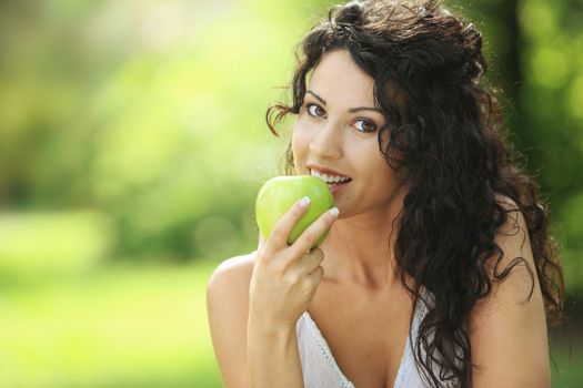 Beautiful cheerful woman eating a green apple, outdoors portrait