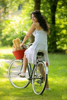 Portrait of a beautiful young woman riding bicycle with groceries in basket