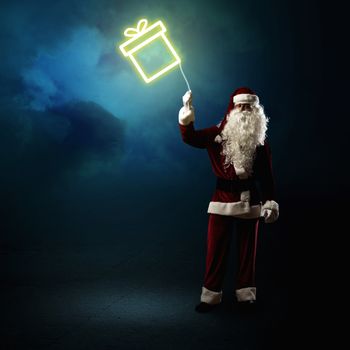 Santa Claus is holding a shining symbol of the gift on a string