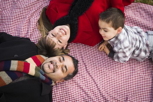 Young Mixed Race Family in Winter Clothing Laying on Their Backs on Picnic Blanket in the Park Together.