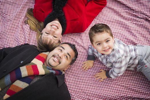 Young Mixed Race Family in Winter Clothing Laying on Their Backs on Picnic Blanket in the Park Together.