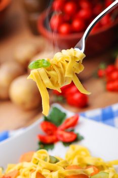 Fork holds tagliatelle with some basil leaves 