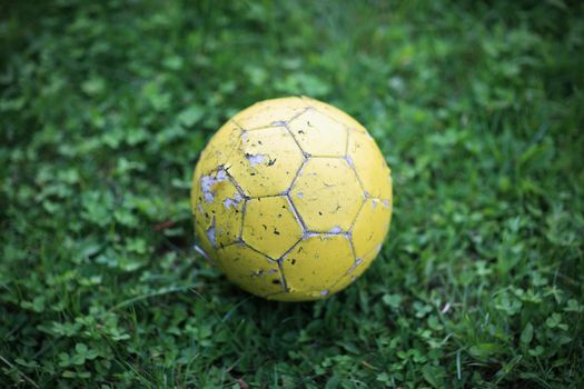 Old yellow soccer ball on green grass