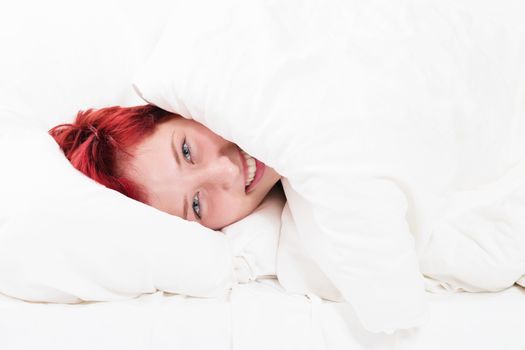 happy redhead woman hiding in bed on white background