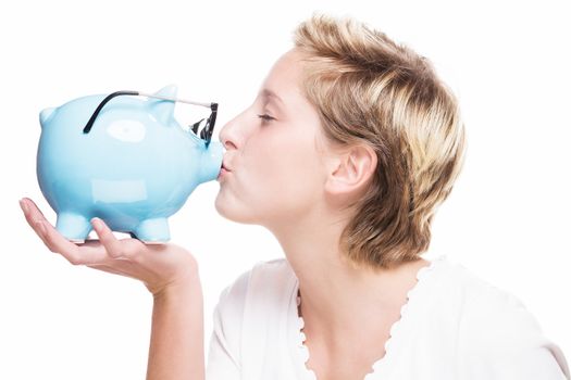 blonde woman kissing a piggy bank which is wearing glasses on white background
