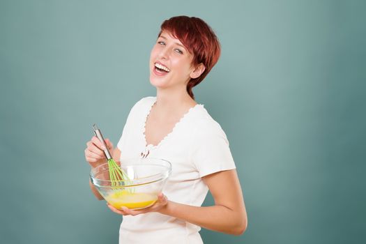 happy redhead woman stirring eggs in a glass bowl