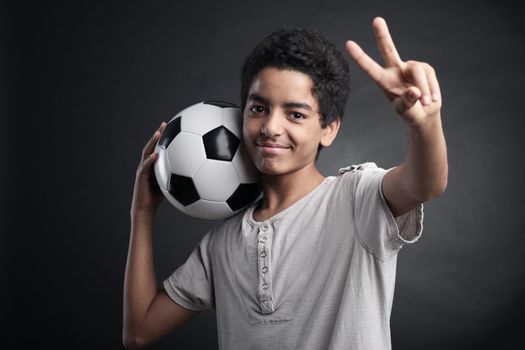 Portrait of young boy with a soccer ball signing victory