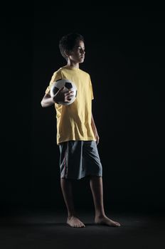 Portrait of young boy with a soccer ball on black background