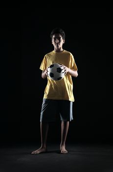 Portrait of young boy with a soccer ball on black background