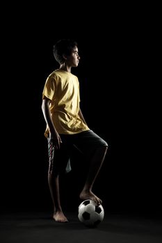 Portrait of young boy with a soccer ball on black background