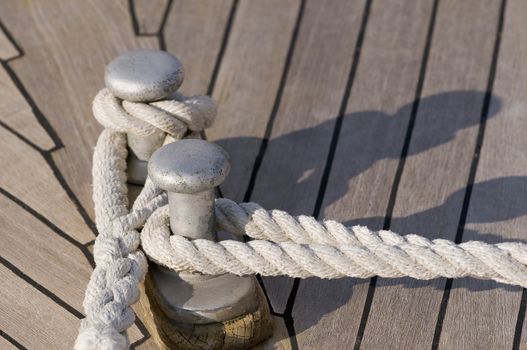 Detail of a teak boat deck: ropes tied up on a bitt 