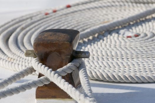 Deck detail of a docked boat with two ropes on a bitt and another one rolled in background