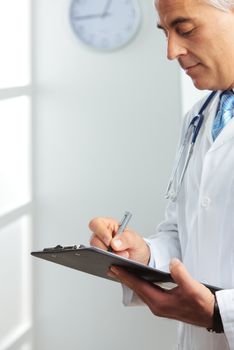 A mature male doctor writing on clipboard 