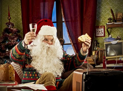 Portrait of Santa Claus watching tv, celebrating with a glass of champagne and panettone