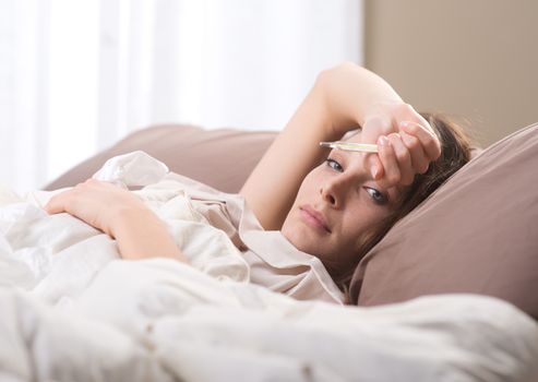 Sick woman with medical thermometer lying on bed