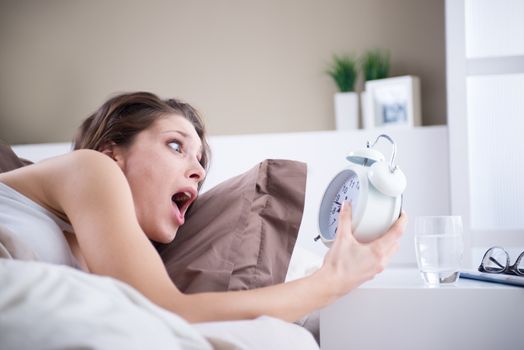 Upset woman holding her alarm clock with an expression of fright