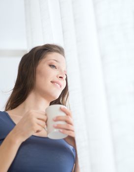 Beautiful woman with cup of coffee looking out of window. 