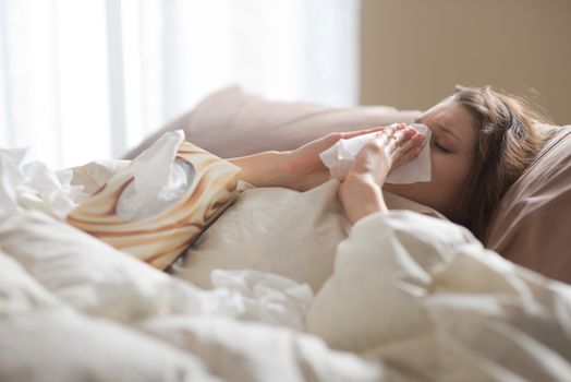 Young sick woman blowing her nose while in bed