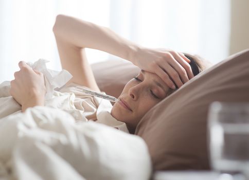 Sick woman with medical thermometer lying on bed