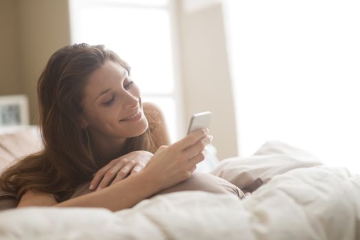 Relaxed woman at home reading a text message in her bright bedroom 