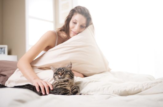 Woman relaxing on bed with her cat on the sunny day. 