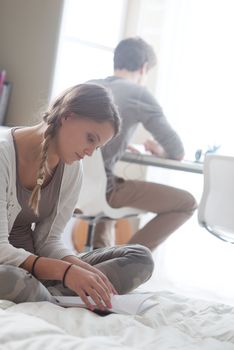 Teen boy and girl at home, sitting and studying. Girl in the foreground.