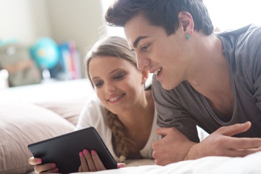 Two happy friends lying in bed using a digital tablet together 