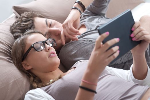 Beautiful teenage couple using digital tablet together while lying in bed at home 