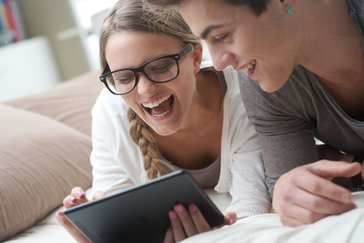 Happy young couple lying on the bed in a bedroom and using digital tablet.