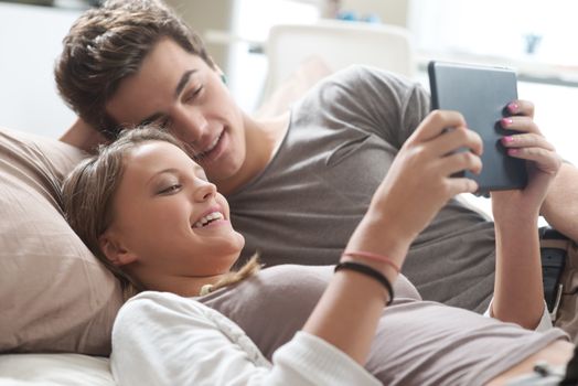 Two happy friends lying in bed using a digital tablet together 