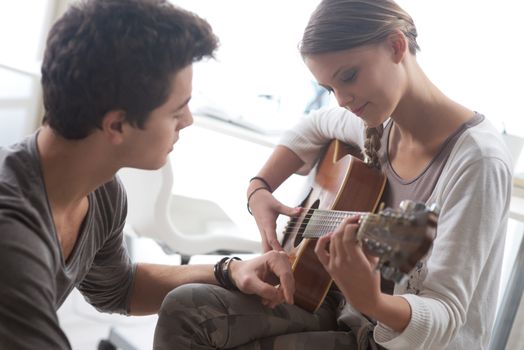 Young beautiful couple resting at home and playing guitar