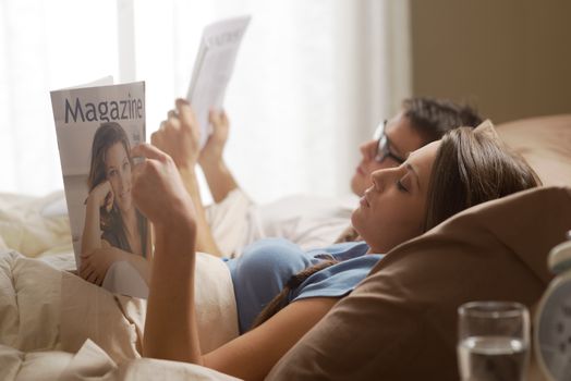 Young couple in bedroom reading newspaper and magazine