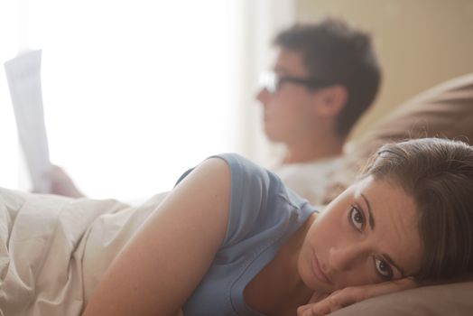 Couple in bed,she's worried while he's reading a newspaper