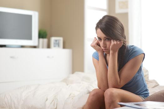 Portrait of young sad woman sitting on bed