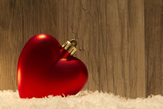 christmas bauble as heart with wooden background and snow 