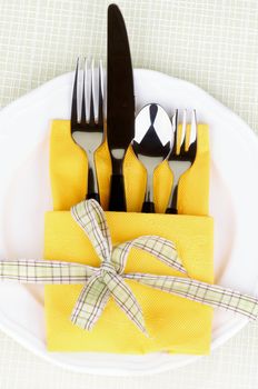 Elegant Table Setting with Fork, Table Knife, Spoon and Dessert Fork into Yellow Napkin Decorated with Green Checkered Bow on White Plate