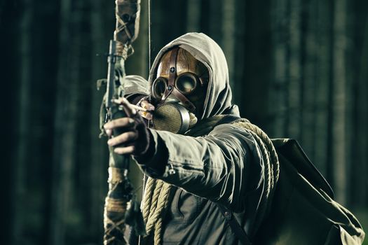 A male bow hunter wearing gas mask, draws back on his bow