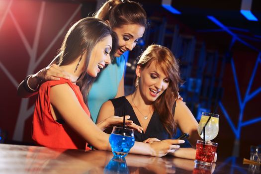 Three beautiful young women friends having fun looking at something funny on their smartphone and laughing