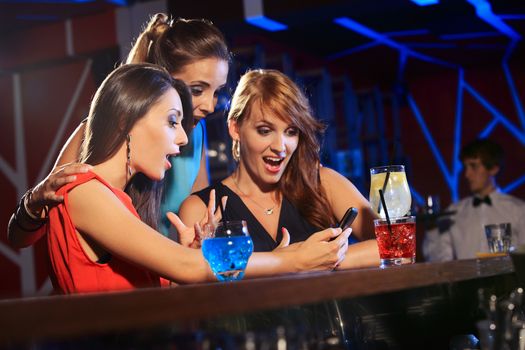 Three beautiful young women friends having fun looking at something funny on their smartphone and laughing