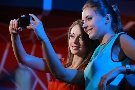 Two happy women at nightclub party taking a self-portrait with smartphone