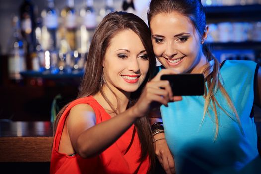 Two happy women at nightclub party taking a self-portrait with smartphone