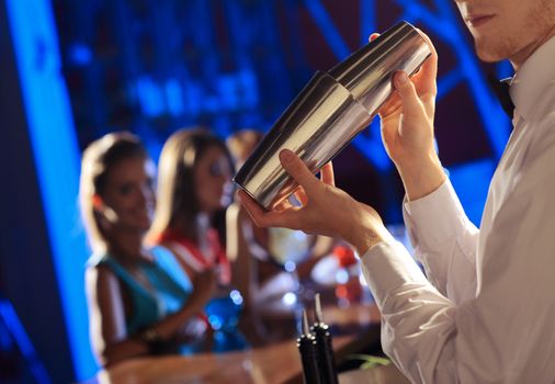 Bartender shaking a cocktail, young women on the background