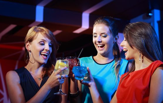 Group of happy beautiful young female friends celebrating in a nightclub with glasses of cocktail in their hands