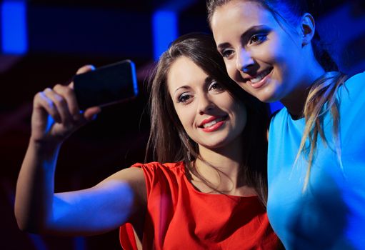 Two happy women at nightclub party taking a self-portrait with smartphone