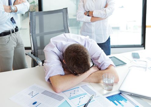 Young office worker is sleeping on the desk, executives behind him