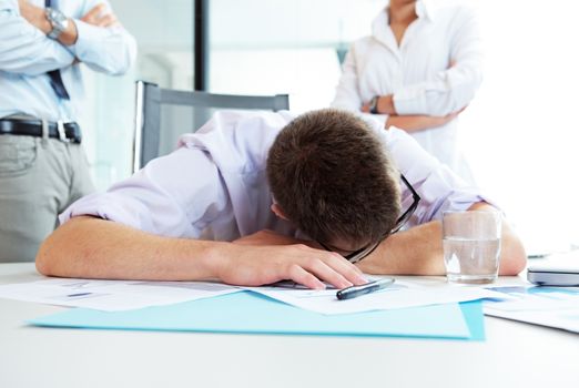Young office worker is sleeping on the desk, executives behind him